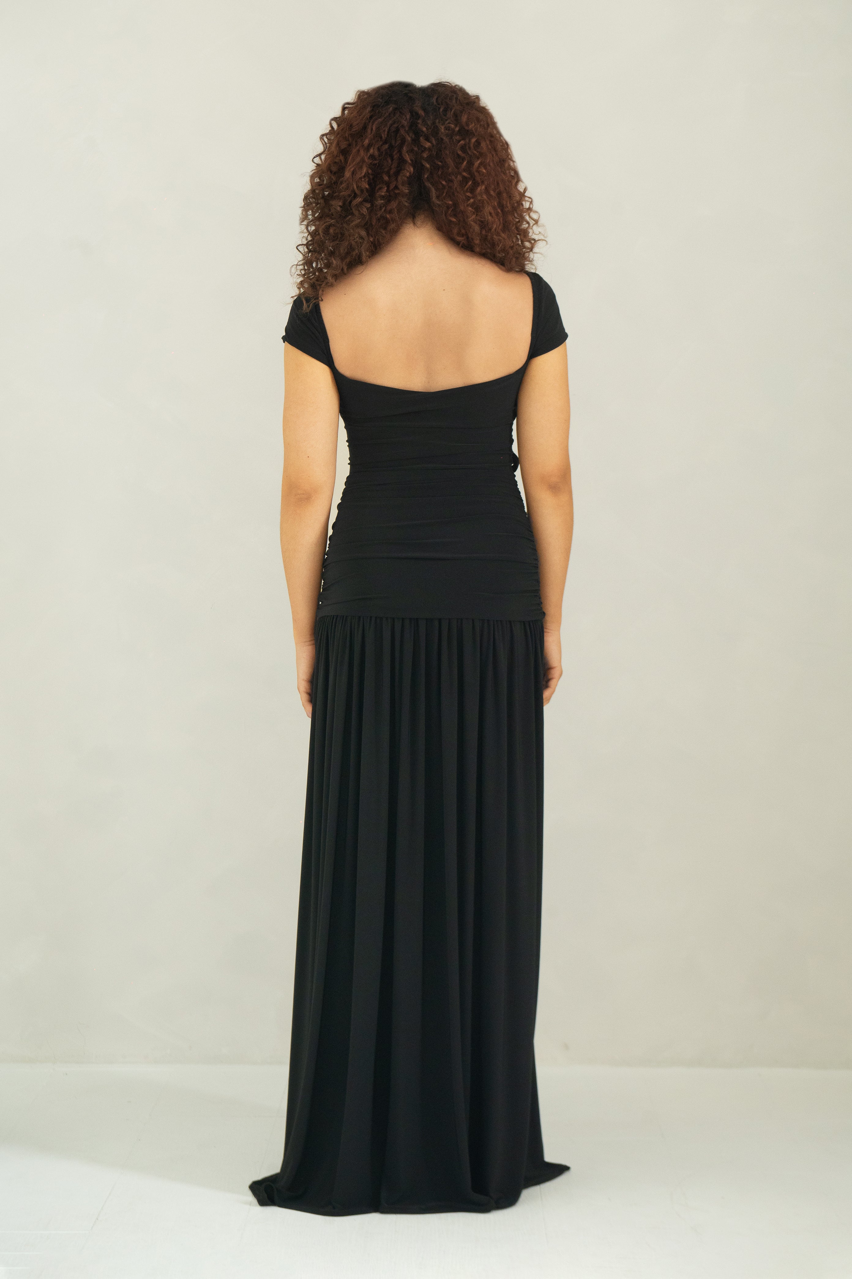 Back view of floor length black dress with cap sleeves, ring detail and front slit